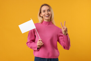 Happy woman with blank white flag showing V-sign on orange background. Mockup for design