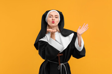 Woman in nun habit blowing kiss against orange background