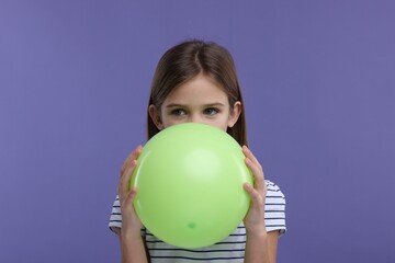 Girl inflating light green balloon on violet background