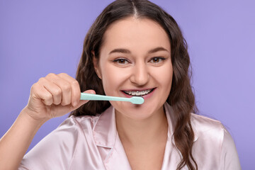 Woman with braces cleaning teeth on violet background