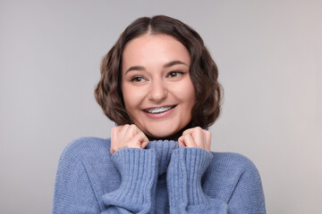 Smiling woman with dental braces in warm sweater on grey background