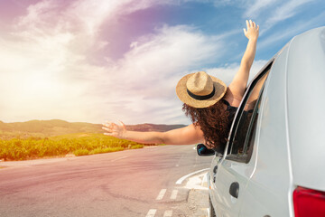 Rearview shot of an young woman leaning out of her car window with her arms outstretched and copy space - obrazy, fototapety, plakaty