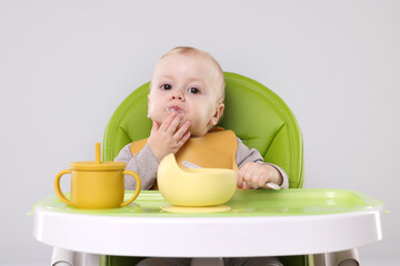 Cute little baby eating healthy food in high chair on gray background