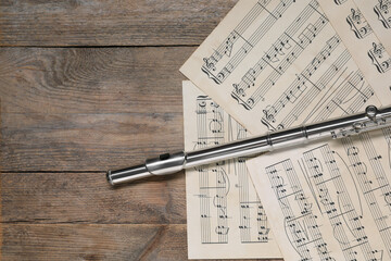 Sheets with musical notes and flute on wooden table, flat lay. Space for text