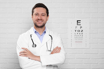 Ophthalmologist near vision test chart on white brick wall - obrazy, fototapety, plakaty