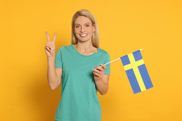 Woman with flag of Sweden showing V-sign on yellow background