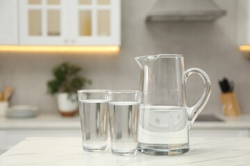 Fototapeta na wymiar Jug and glasses with clear water on white table in kitchen