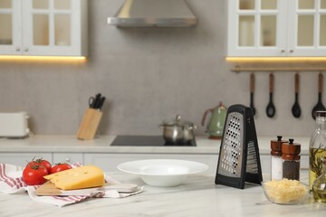 Grater, delicious cheese and other products on white marble table in kitchen