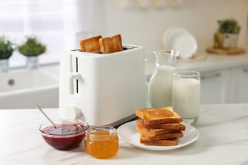 Making toasts for breakfast. Appliance, crunchy bread, honey, jam and milk on white marble table in kitchen