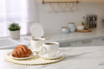 Fototapeta na wymiar Breakfast served in kitchen. Cups of coffee and fresh croissant on white marble table. Space for text