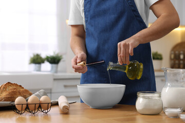 Making bread. Man pouring oil into bowl at wooden table in kitchen, closeup
