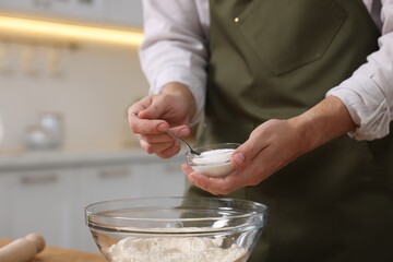 Making bread. Man putting salt into bowl with flour at table in kitchen, closeup