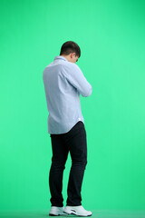 A man, full-length, on a green background, looks at his watch