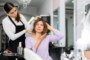 Fototapeta premium Skilled young female hairdresser offering modern hairstyling to woman client visiting professional hair salon..