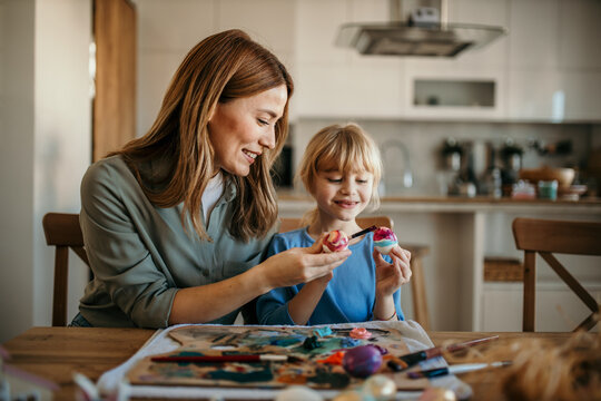Smiling mom and daughter engaged in the creative process of preparing Easter eggs with vibrant colors