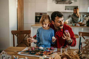 Joyful father and daughter engaged in Easter egg decorating, sharing smiles and laughter