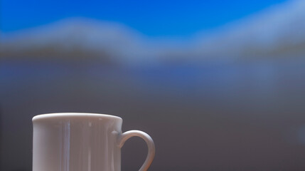 Close-up view, white coffee cup on wooden counter and smart phone, note book put on digital tablet by window, coffee break and relax after work in cafe with a reading book in the background