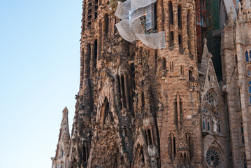 Closeup of Sagrada Familia's exterior in Barcelona, showcasing its Gothic and Art Nouveau style with detailed sculptures and spires. Construction netting hints at ongoing work.