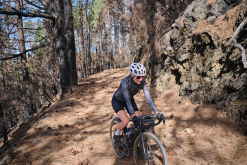 Young woman cyclist wearing cycling kit and helmet riding a gravel bike on gravel path. Biking...