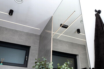 LED light strips mounted in the wall and ceiling in a modern bathroom, visible ventilation...