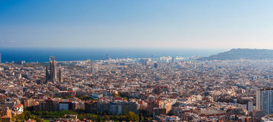 Panoramic view of Barcelona's skyline featuring the Sagrada Familia under a clear sky, with the Mediterranean Sea and port visible, showcasing the city's mix of architecture and natural landscape.
