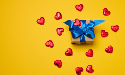 Box tied with a blue ribbon and small hearts on a yellow background, top view