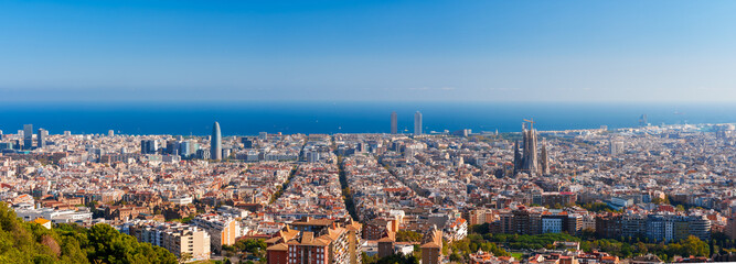 Panoramic view of Barcelona, Spain, showcasing the Eixample district's grid layout, the Sagrada Familia's spires, and the blend of modern and historical architecture against the Mediterranean Sea.