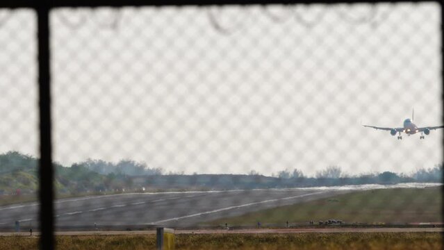 Footage of an airplane with an unrecognizable livery, landing, touching and braking. View of the runway through the airport fence. Airstrip