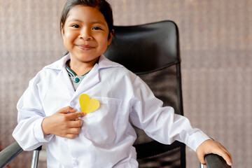 Little girl in a medical gown holding a yellow paper heart in her hand. Selective focus. Copyspace.