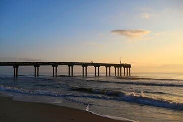 Fototapeta na wymiar Sunrising over a pier and beach on the Atlantic Ocean