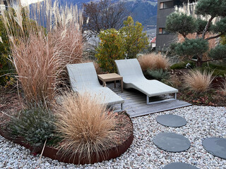 Modern garden design: two loungers idyllically surrounded by grasses and perennials, in the foreground round slabs laid in gravel