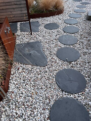 Modern garden design: round slabs laid in pebbles and a faucet in a rusty metal plate