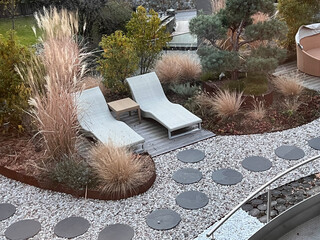 Modern garden design: two loungers idyllically surrounded by grasses and perennials, in the foreground round slabs laid in gravel and a barefoot path