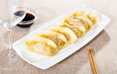 Hearty dinner is prepared on plate - portion of boiled gyoza dumplings served with bowl of soy sauce and chopsticks. Traditional oriental culinary art, acquaintance with culture through national