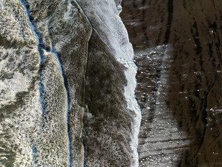 Aerial: Abstract texture of sea foam from above. Bethells Beach, Auckland, New Zealand.