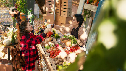 Female client and vendor drinking cup of hot coffee at farmers market, woman buying fresh eco...