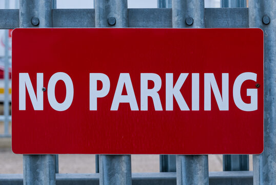 Red no parking sign with white text on a metal fence