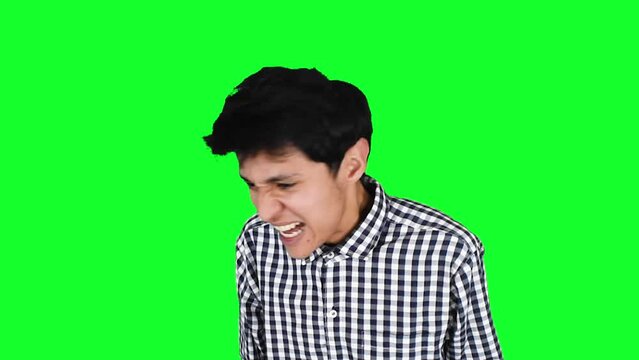 Joven hombre caucasico delgado con camisa a cuadros sobre un fondo verde enojado furioso y lleno de coraje 