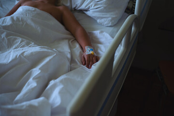 The hand of a lonely little child with a catheter lying in a hospital room on a bed in the dark