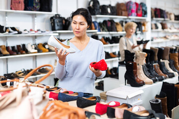 Focused Asian woman who came to a shoe store for shopping, chooses ballet flats, carefully examining them