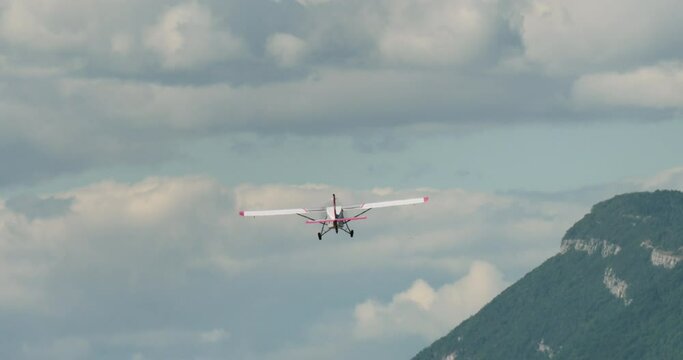 A light aircraft flies over rugged mountainous terrain, with a clear sky in the background and visible rocky textures