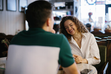 A couple has fun chatting over morning coffee in a cafe. A girl laughs at her boyfriend's jokes.