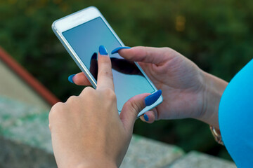 Close up view of woman in blue with blue nails typing sms on smart phone