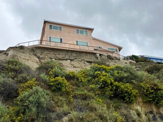 A home perches dangerously on edge of cliff, with foundation exposed and partially eroded