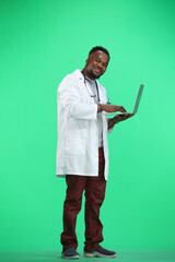 The doctor, in full height, on a green background, uses a laptop