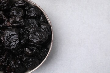 Sweet dried prunes in bowl on light table, top view. Space for text