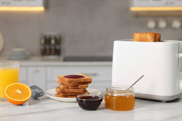 Making toasts for breakfast. Appliance, crunchy bread, honey, jam and orange fresh on white table in kitchen