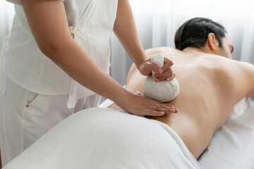 Hot herbal ball spa massage body treatment, masseur gently compresses herb bag on man body. Tranquil and serenity of aromatherapy recreation in day lighting ambient at spa salon. Quiescent - obrazy, fototapety, plakaty