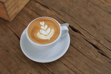 Hot latte with latte art in white cup on wooden table in coffee shop.  Fresh morning coffee with delicious milk foam.
