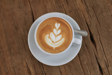 Hot latte with latte art in white cup on wooden table in coffee shop.  Fresh morning coffee with delicious milk foam.